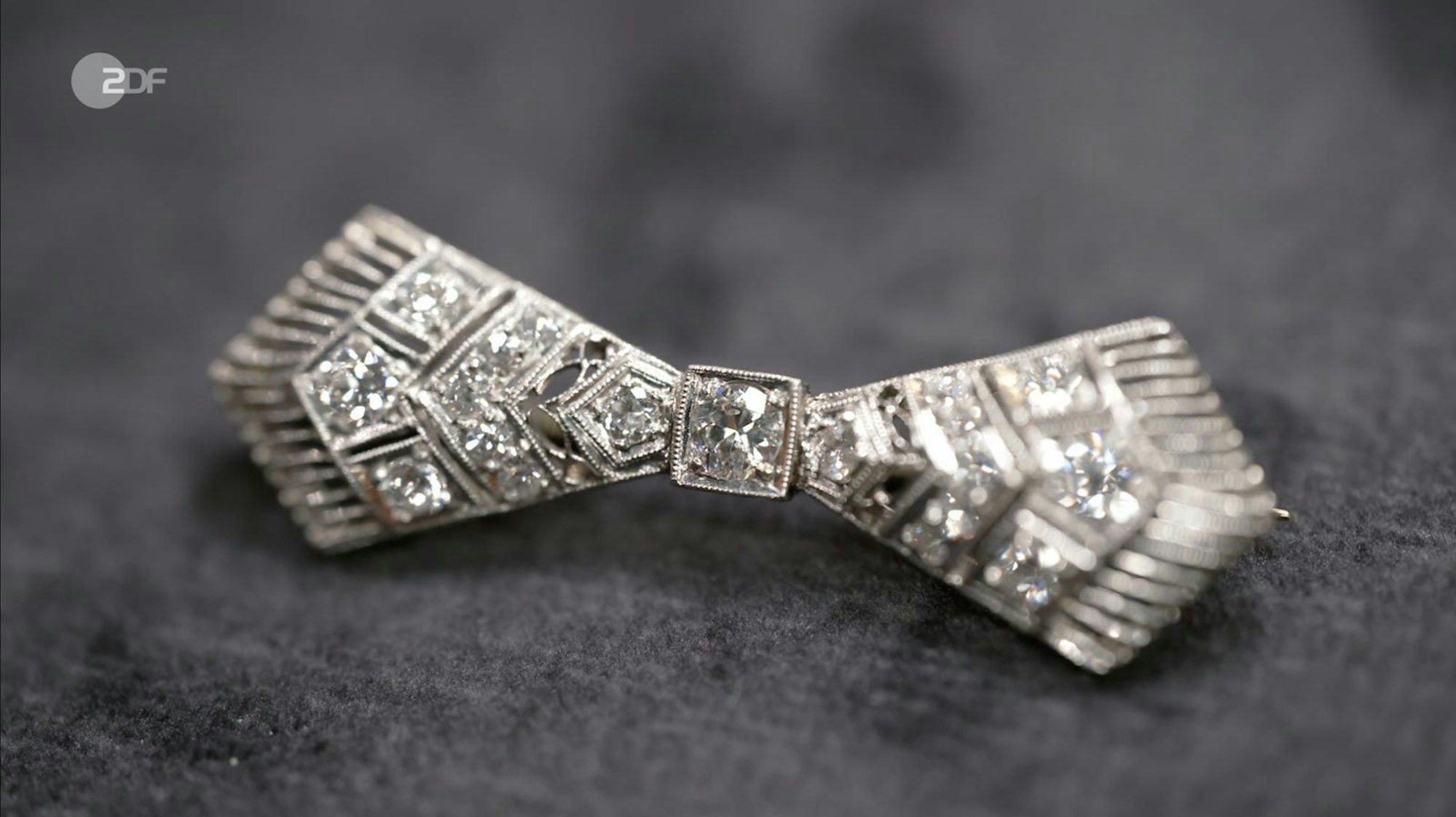 Eine Schleifenbrosche bezeichnete Patrick Lessmann als geometrischen Art-déco-Schmuck, den er in den 1930er-Jahren datierte. Für die Brosche mit Diamanten (1,1 Karat) aus Platin wünschte sich die Verkäuferin 400 Euro, der Experte taxierte 900 bis 1.100 Euro und Susanne Steiger zahlte 1.000 Euro. (Bild: ZDF)