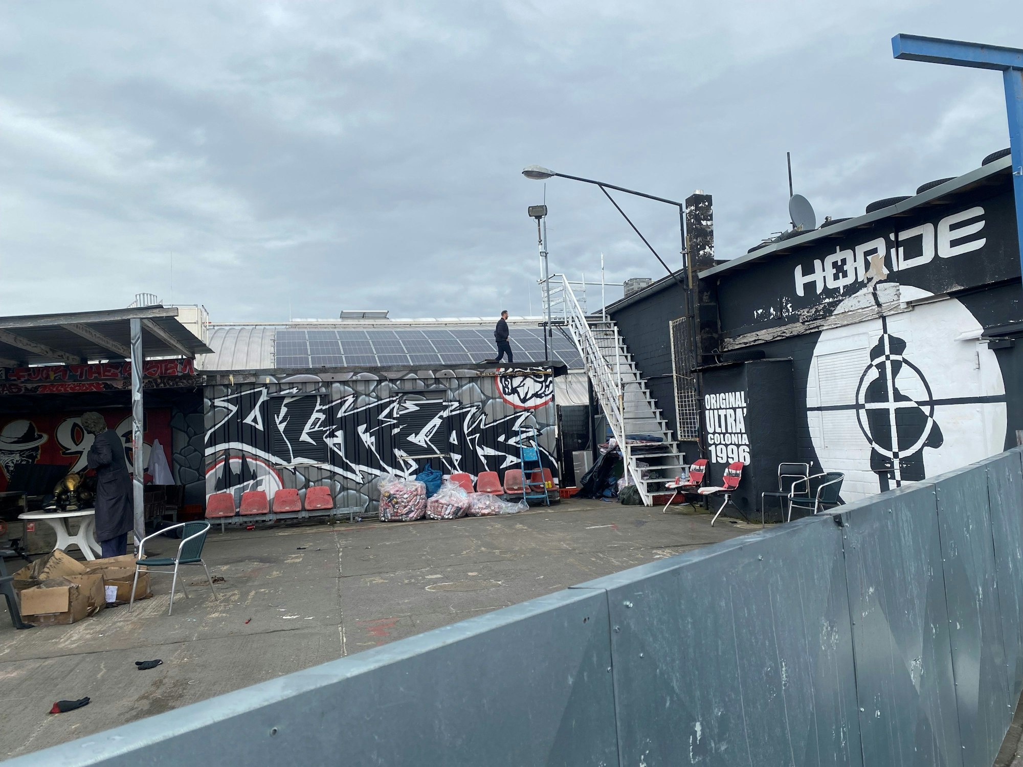 Die Halle der RheinStars (hinten) grenzt an das Hauptquartier der „Wilden Horde“. Eine Person ist bei einer Begehung zu sehen.