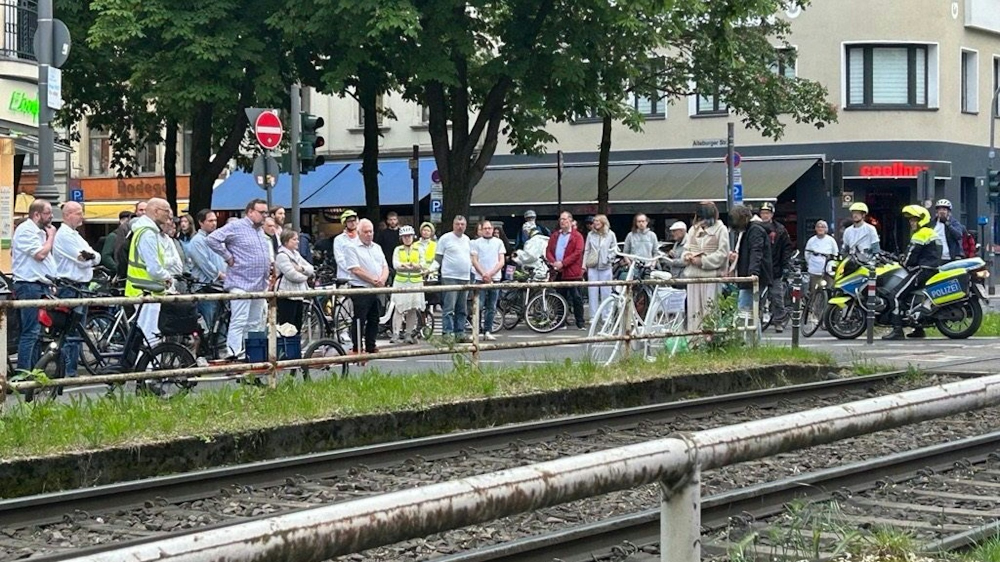 Zahlreiche Menschen stehen vor einem weißen Fahrrad, das an einem Bahnübergang steht.