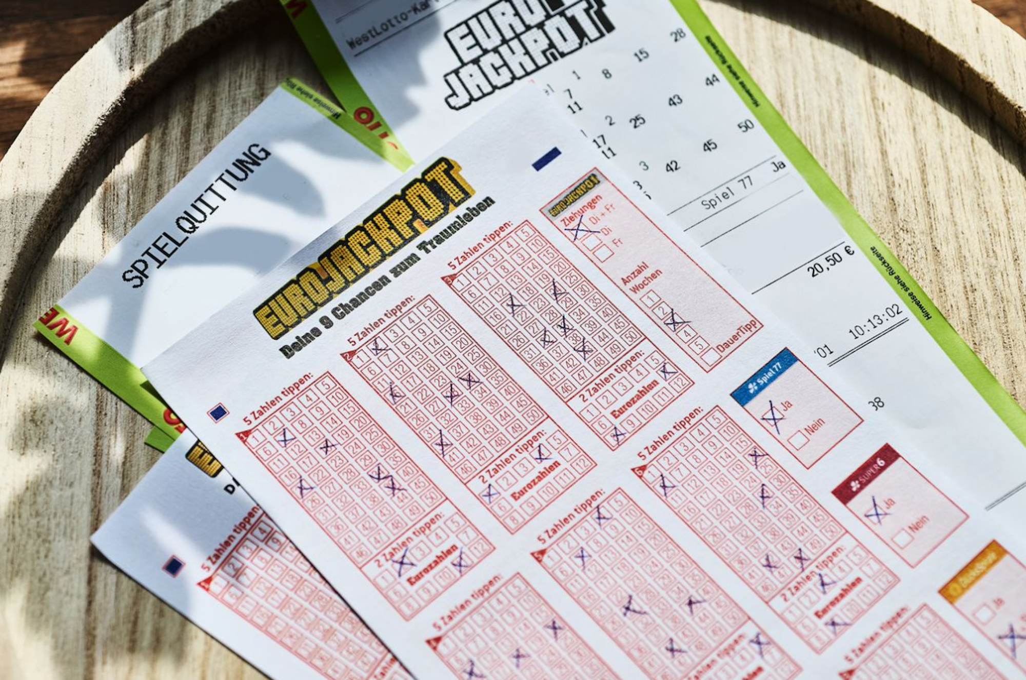 Auf einem Tisch liegen ein Eurojackpot Tippschein und eine Spielquittung.