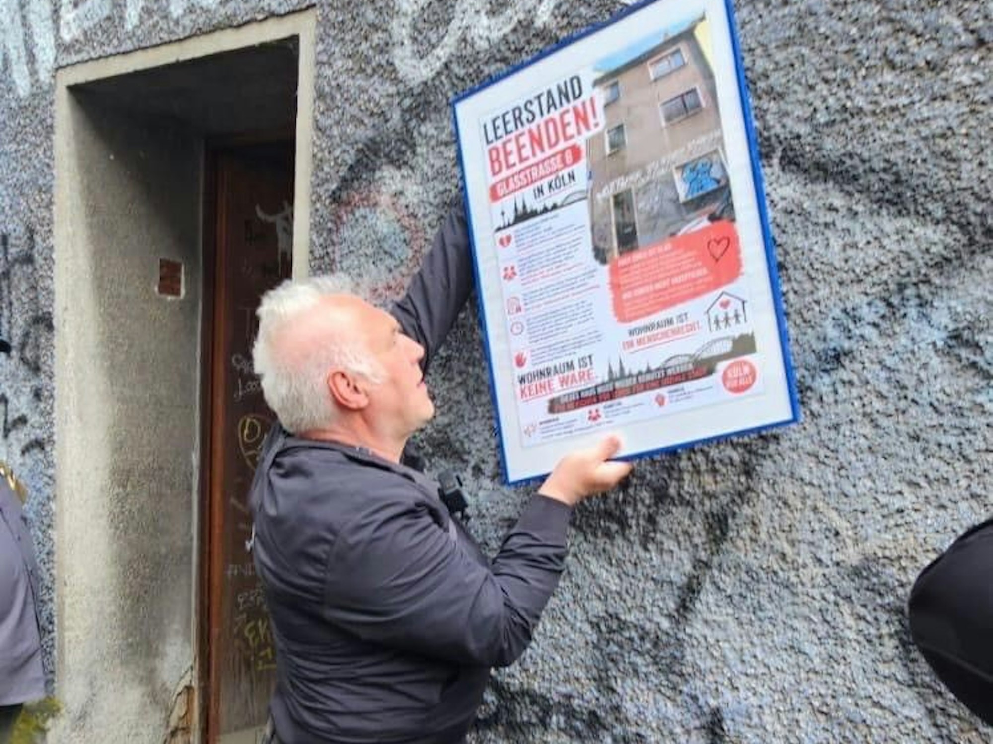Kalle Gerigk hängt ein Plakat an einer Hauswand auf.