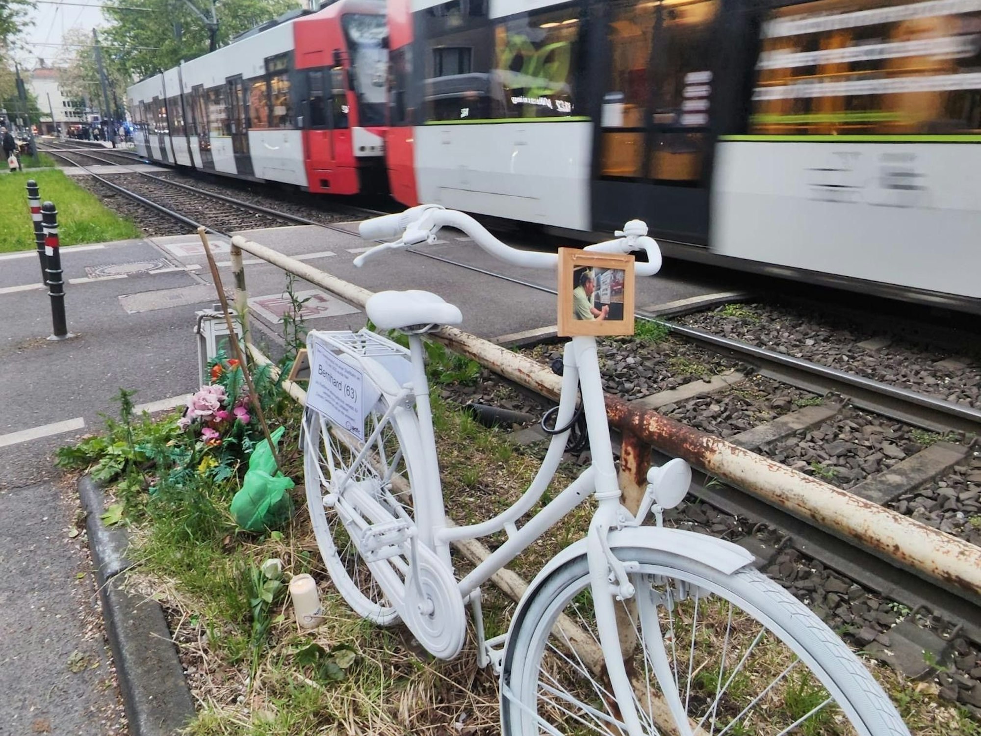 Ein weiß lackiertes Fahrrad steht an einem Bahnübergang während ein Zug vorbeirauscht.
