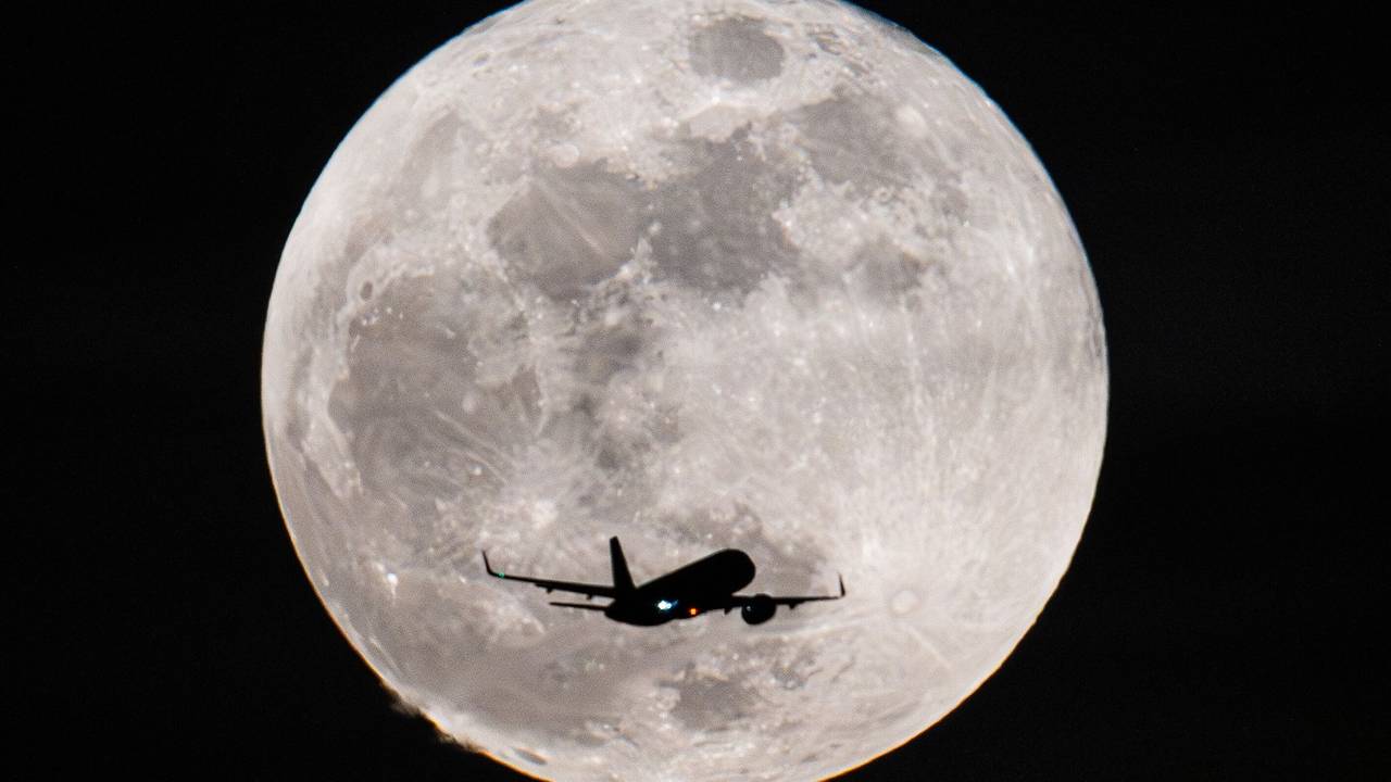 Ein Passagierflugzeug fliegt am Vollmond vorbei