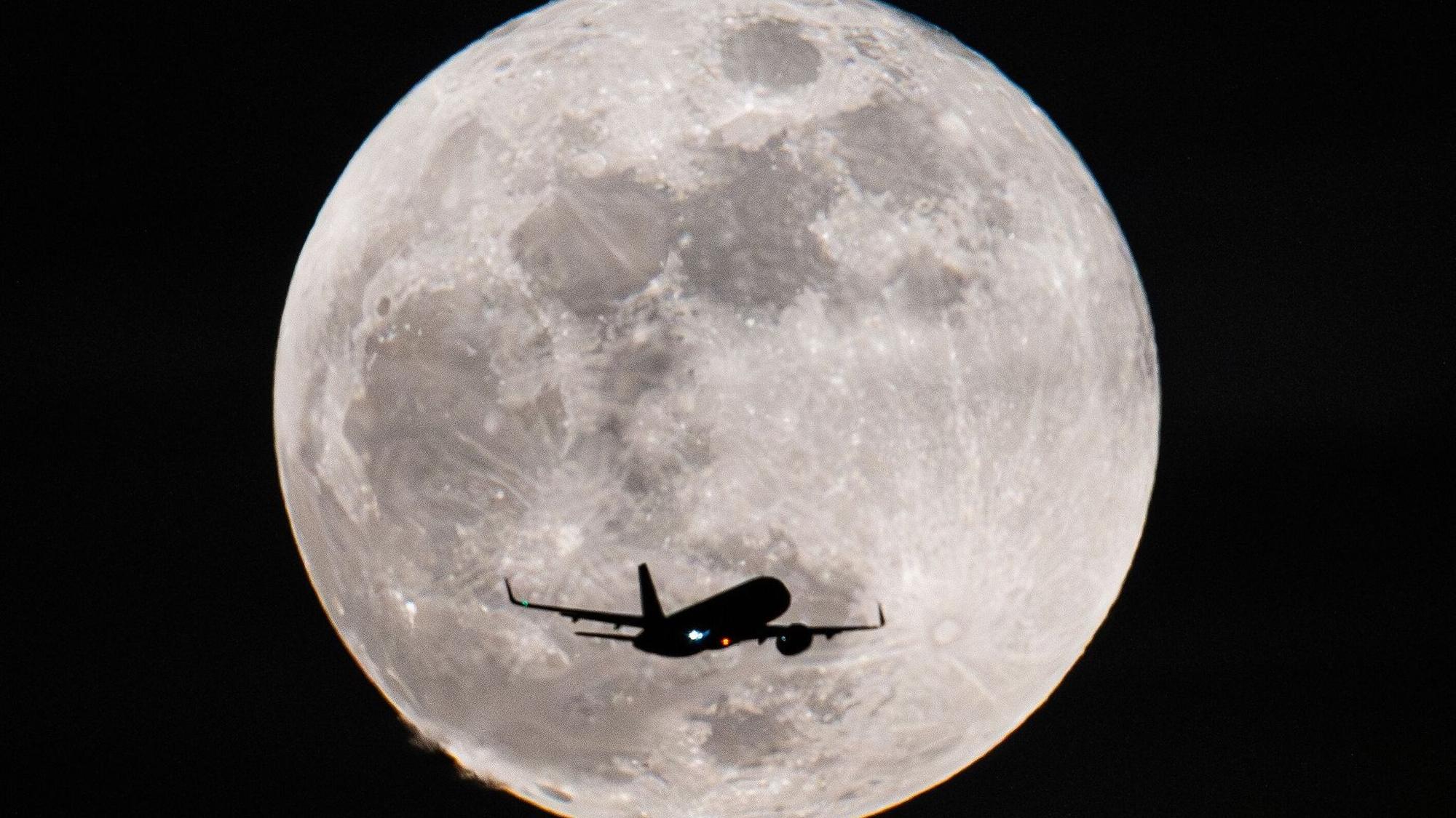 Ein Passagierflugzeug fliegt am Vollmond vorbei