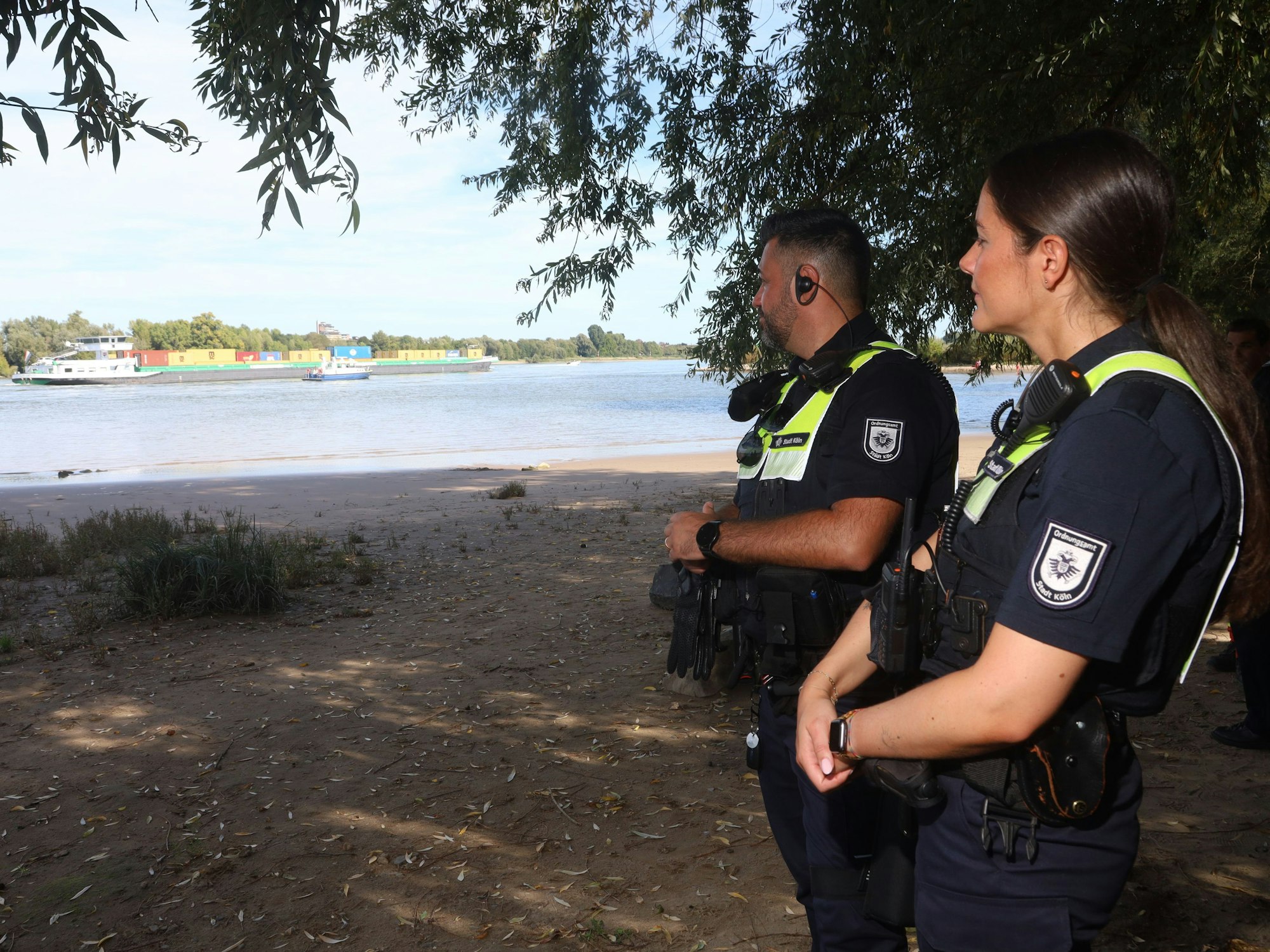 Zwei Mitarbeitende des Ordnungsdienstes der Stadt Köln blicken auf den Rhein.