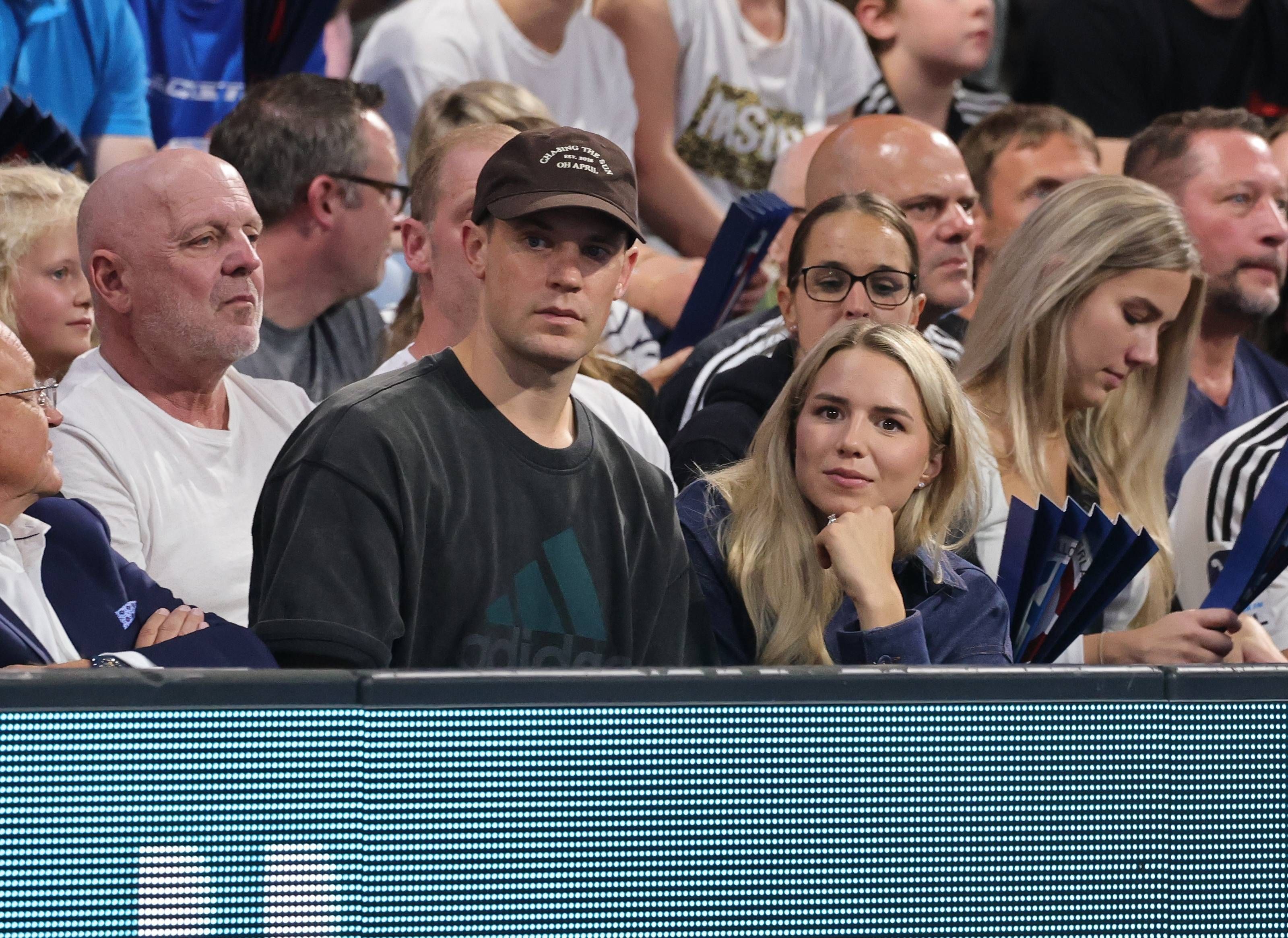 Anika Bissel und Manuel Neuer sitzen gemeinsam auf der Tribüne bei einem Handballspiel