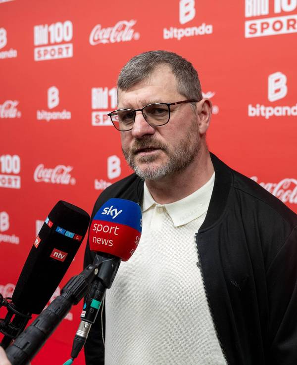 Fußballtrainer Steffen Baumgart steht vor mehreren Mikrofonen bei einer Veranstaltung.