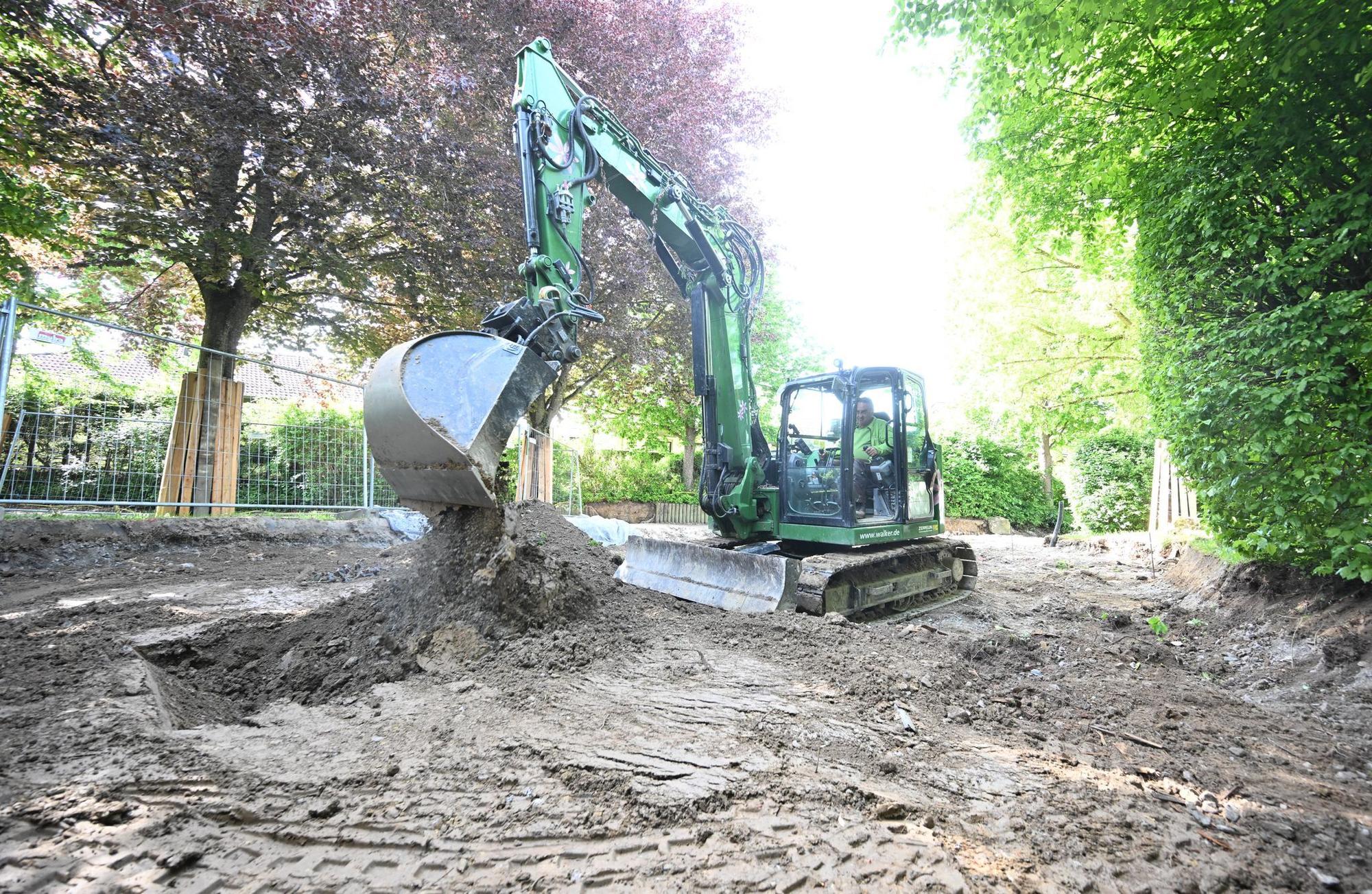 Ein Bagger gräbt auf einer Baustelle in einem Garten ein Loch.