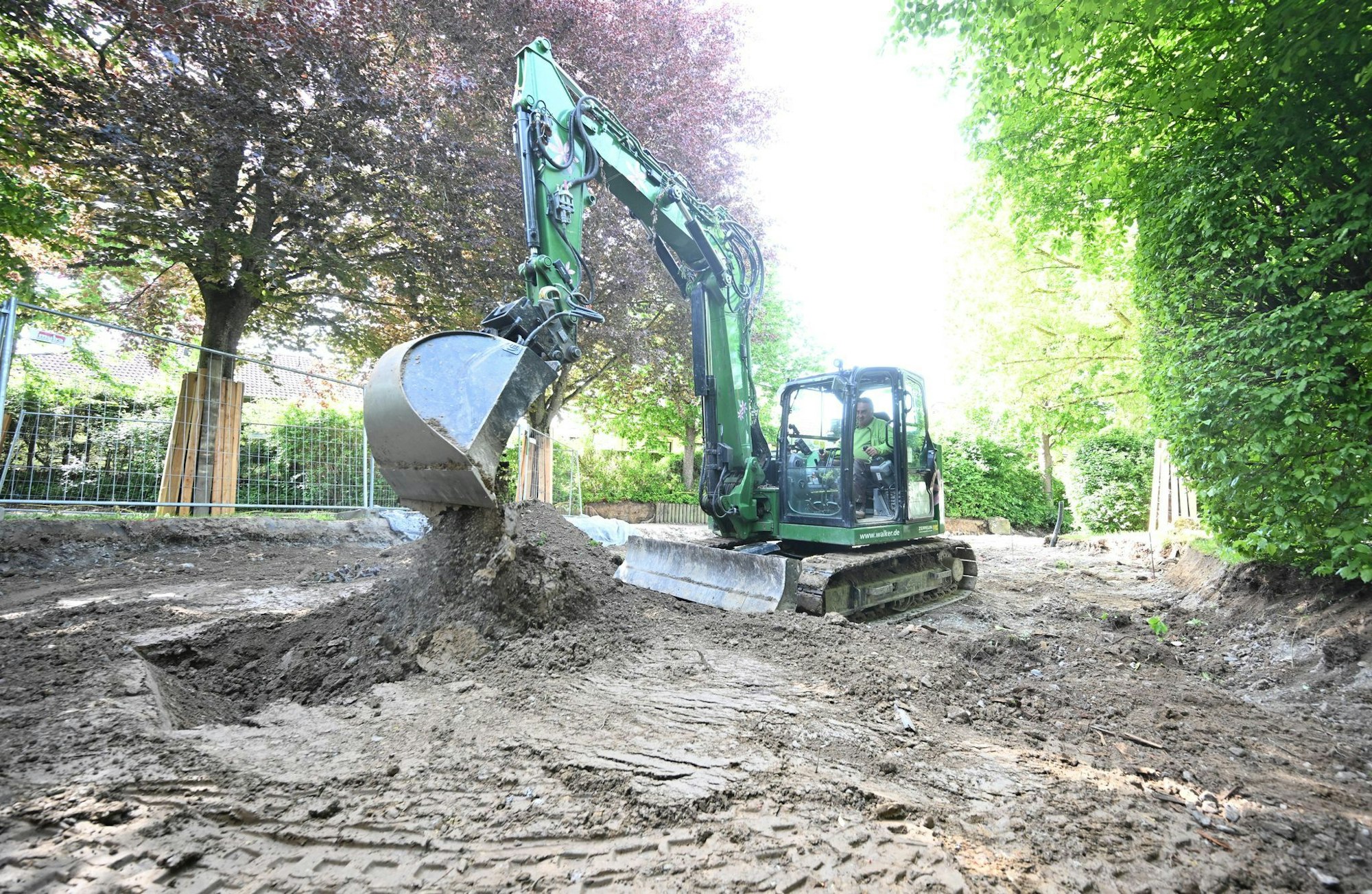 Ein Bagger gräbt auf einer Baustelle in einem Garten ein Loch.
