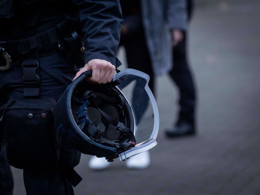 Hand eines Polizisten hält Schutzhelm und Handschellen