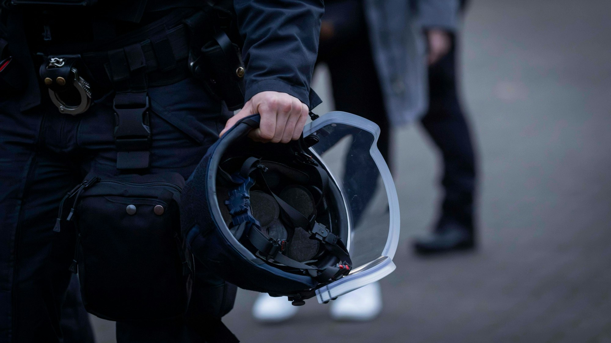 Hand eines Polizisten hält Schutzhelm und Handschellen