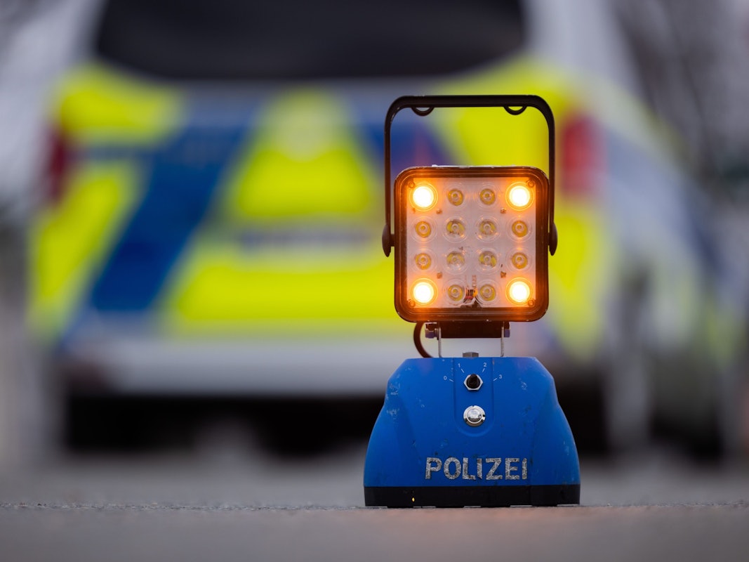 Ein Warnlicht mit der Aufschrift „Polizei“ steht auf der Straße vor einem Einsatzfahrzeug der Polizei.