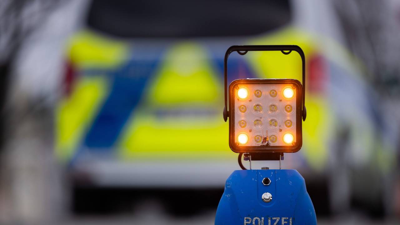 Ein Warnlicht mit der Aufschrift „Polizei“ steht auf der Straße vor einem Einsatzfahrzeug der Polizei.
