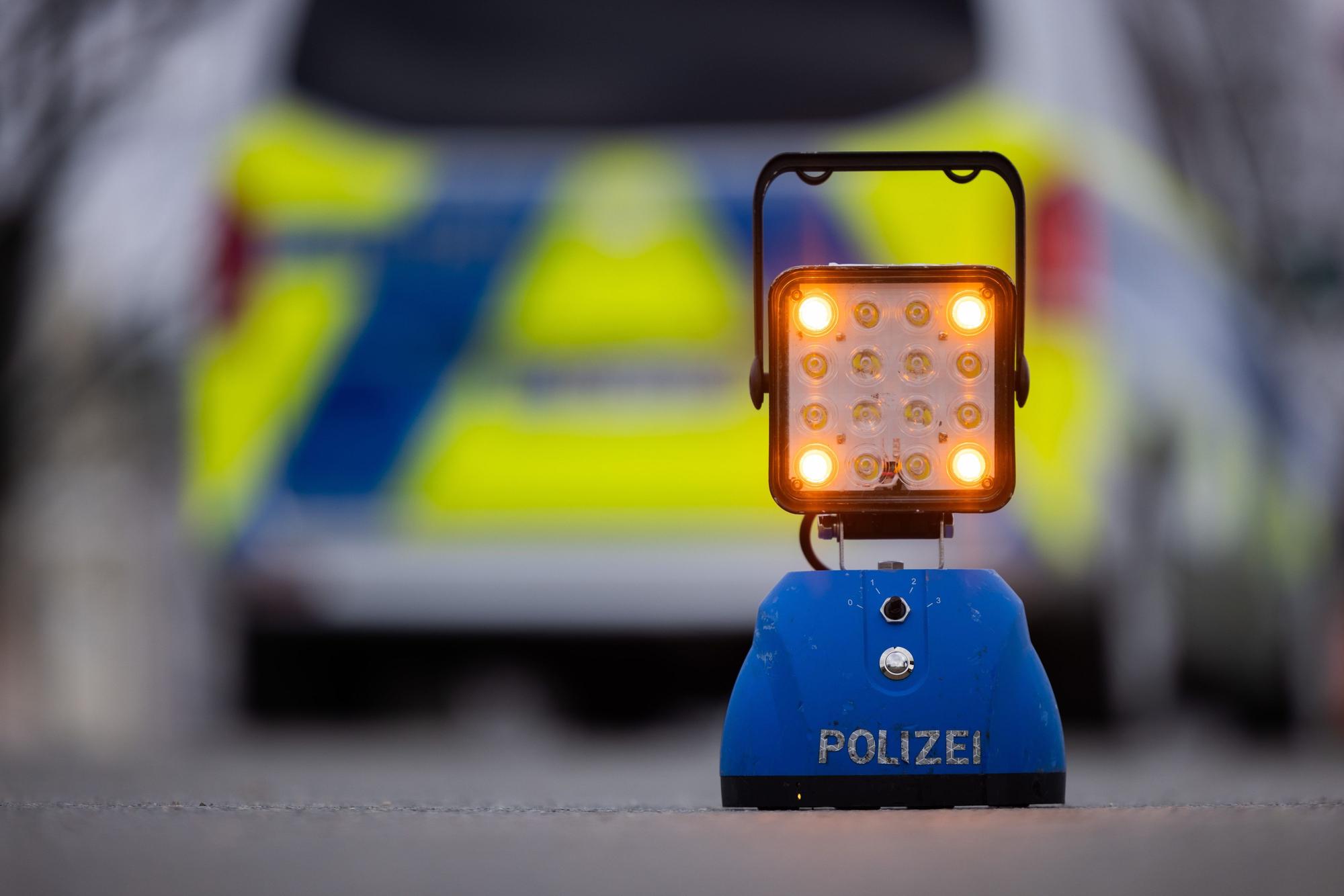 Ein Warnlicht mit der Aufschrift „Polizei“ steht auf der Straße vor einem Einsatzfahrzeug der Polizei.