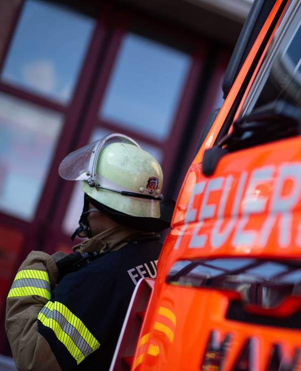 Eine Einsatzkraft der Feuerwehr steht neben einem Einsatzfahrzeug der Feuerwehr.