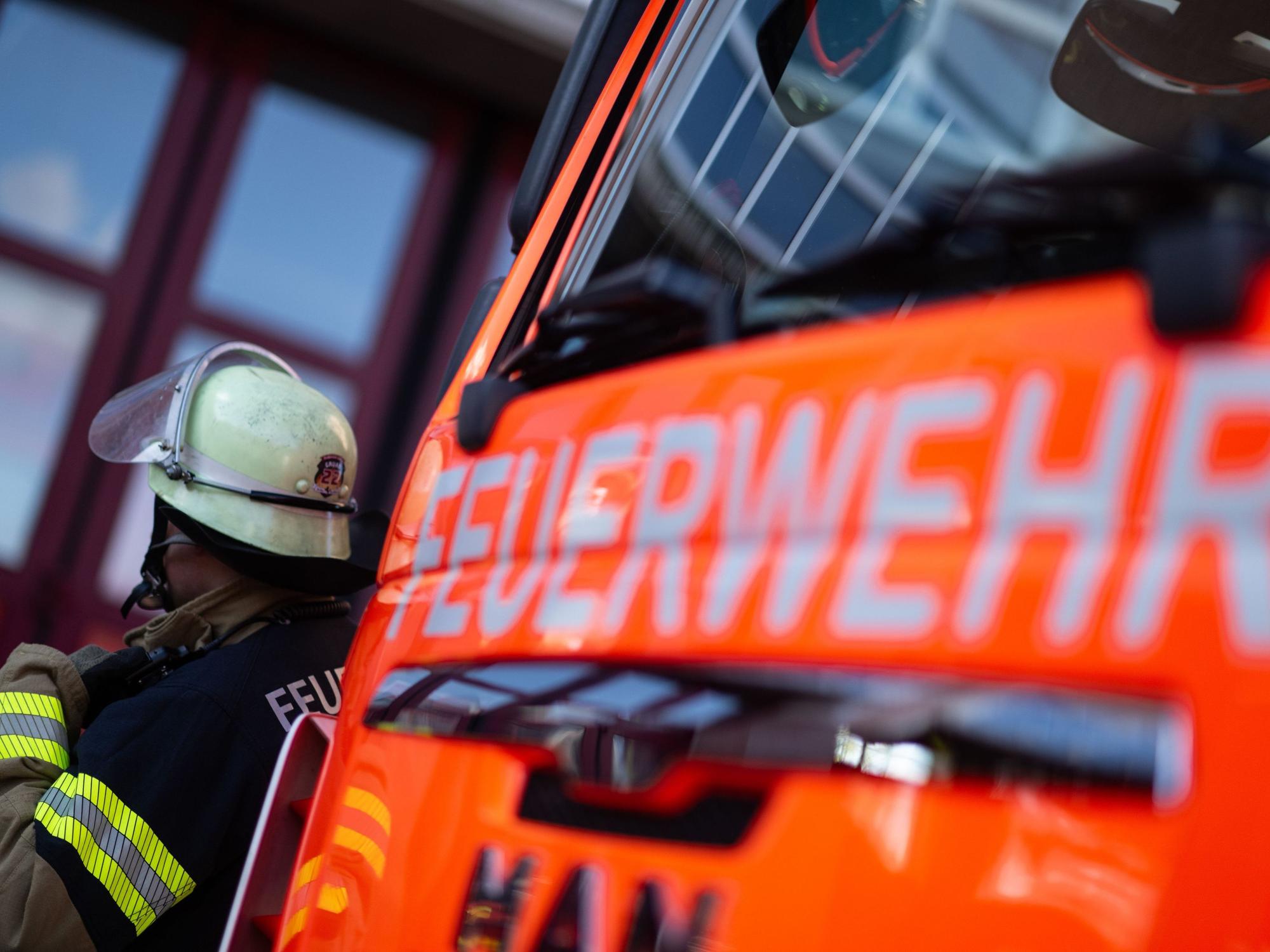 Eine Einsatzkraft der Feuerwehr steht neben einem Einsatzfahrzeug der Feuerwehr.