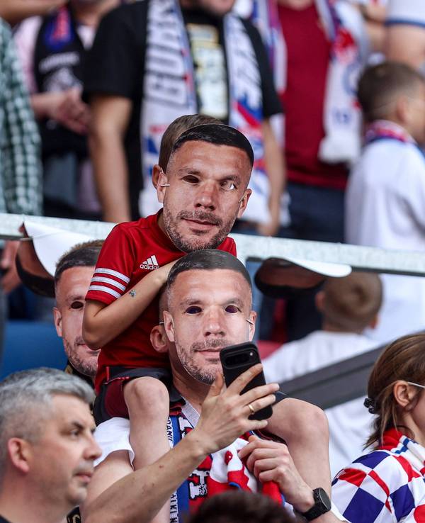 Zwei Fans mit Poldi-Masken auf der Tribüne.