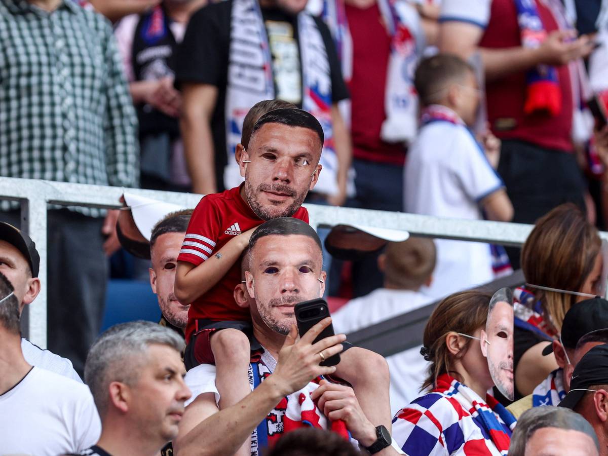 Zwei Fans mit Poldi-Masken auf der Tribüne.