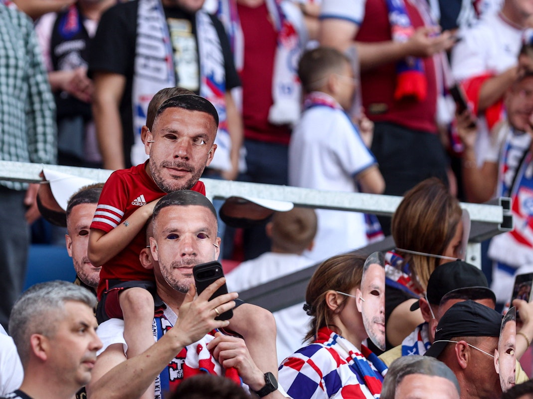Zwei Fans mit Poldi-Masken auf der Tribüne.