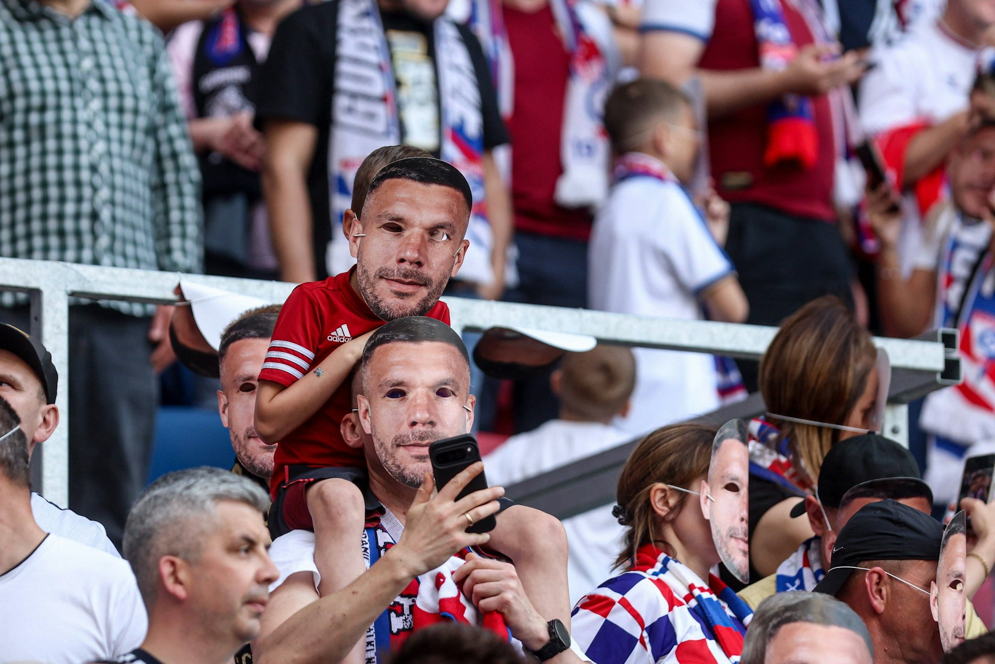 Zwei Fans mit Poldi-Masken auf der Tribüne.