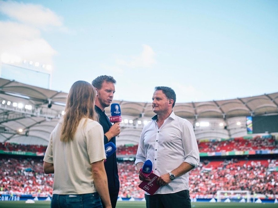 Moderator Thomas Wagner steht mit seinem Mikrofon am Spielfeldrand und spricht mit Julian Nagelsmann.