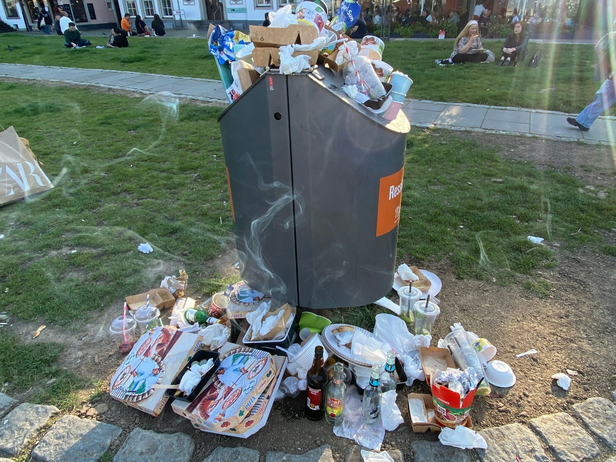 Um einen überquellenden Mülleimer liegt Müll.