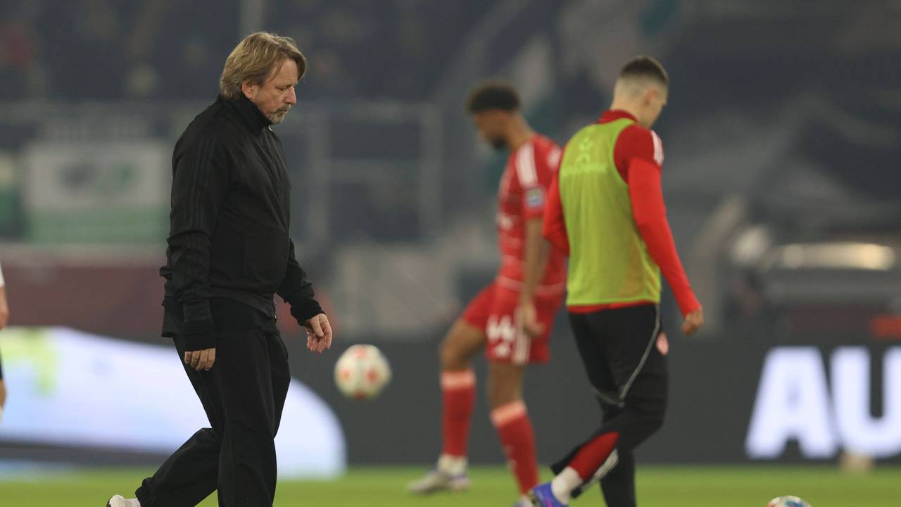 Sven Mislintat geht mit enttäuschtem Blick über den Rasen. Im Hintergrund sieht man zwei Spieler der Fortuna, die sich aufwärmen.