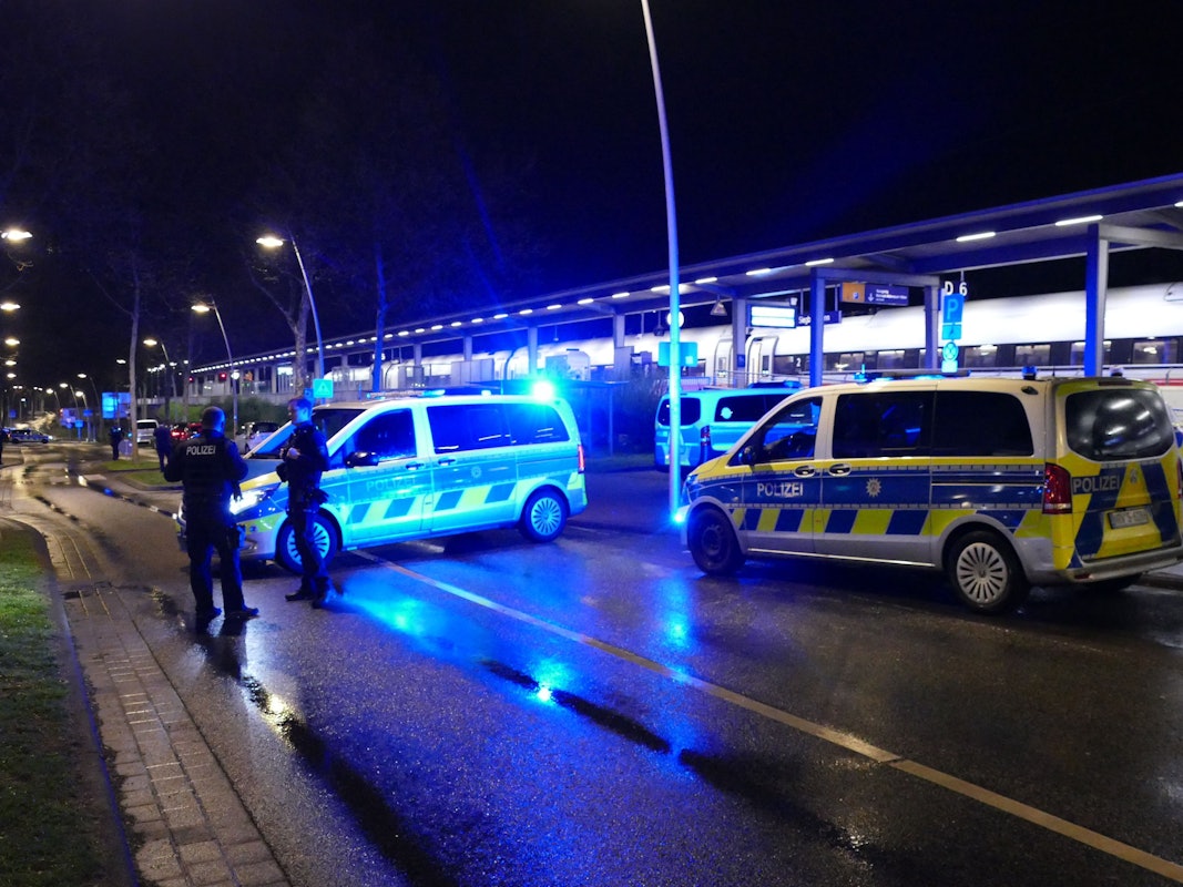 Polizeiautos mit Blaulicht stehen neben den Gleisen des Bahnhofs Siegburg, wo ein ICE hält.