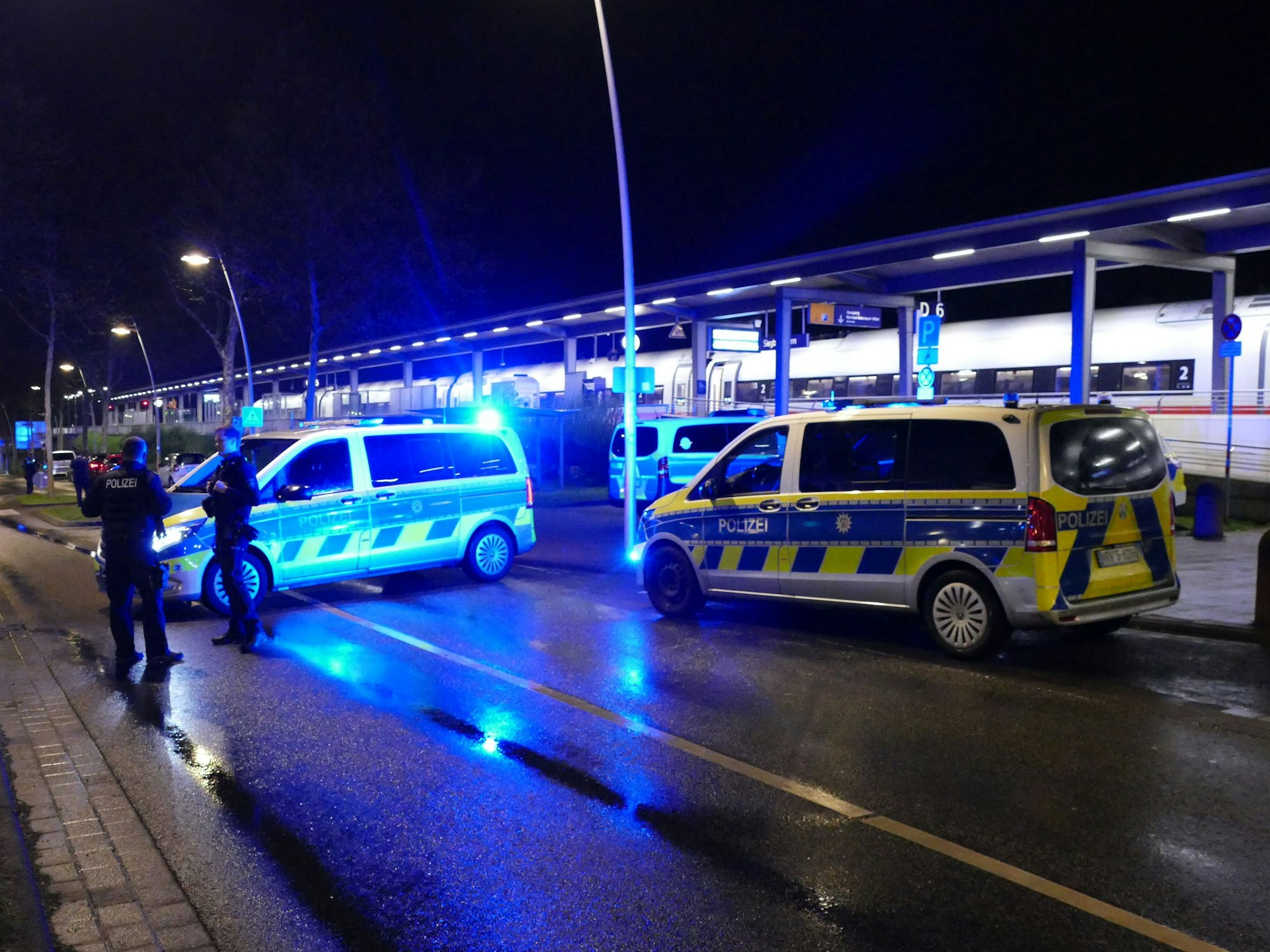 Polizeiautos mit Blaulicht stehen neben den Gleisen des Bahnhofs Siegburg, wo ein ICE hält.