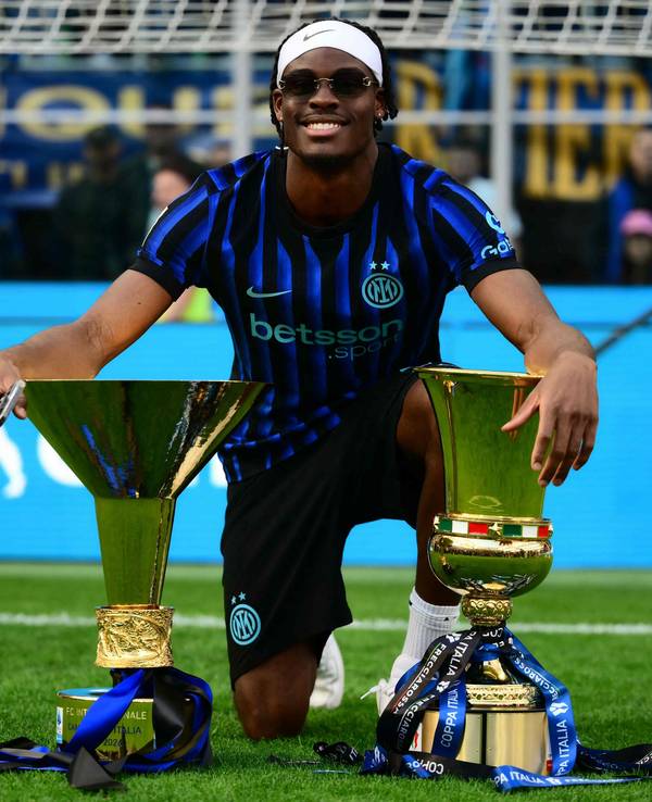 Yann Aurel Bisseck posiert auf dem Rasen mit zwei Trophäen.