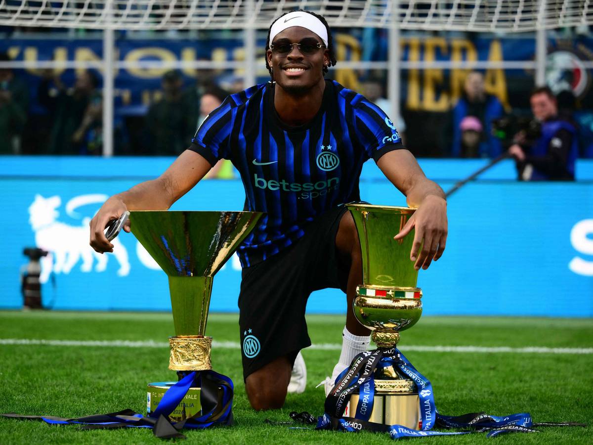 Yann Aurel Bisseck posiert auf dem Rasen mit zwei Trophäen.