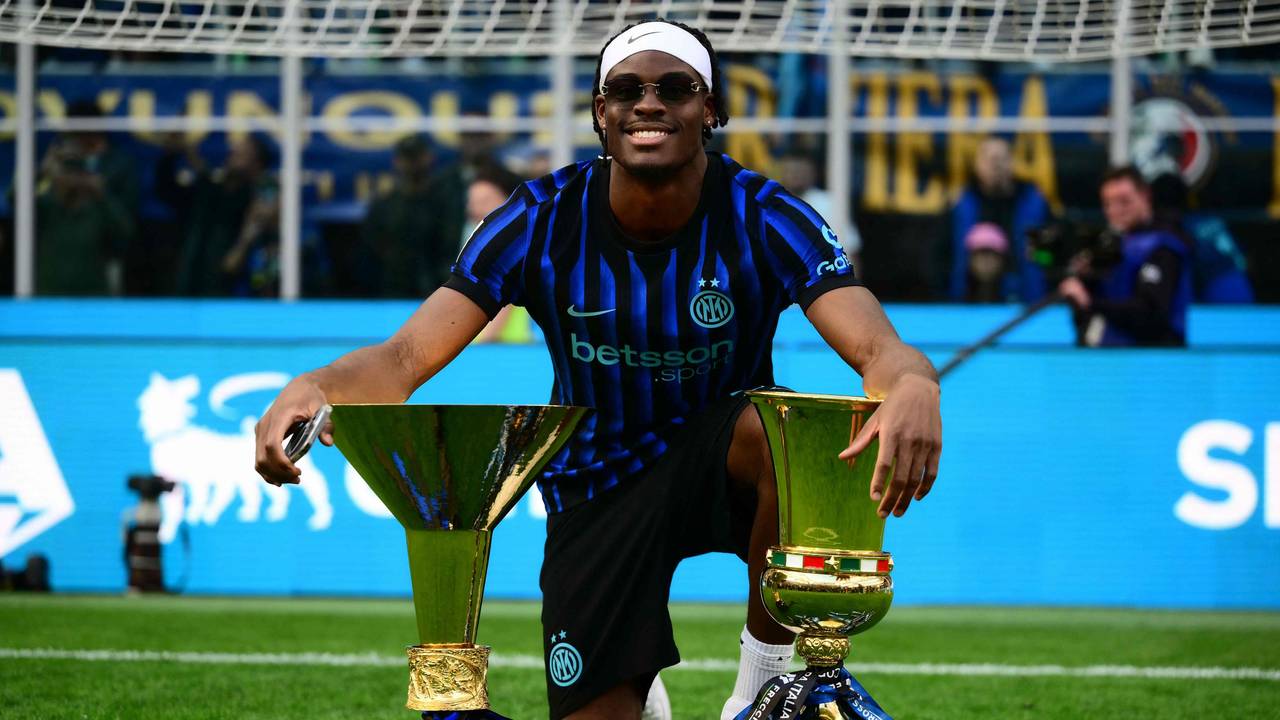 Yann Aurel Bisseck posiert auf dem Rasen mit zwei Trophäen.