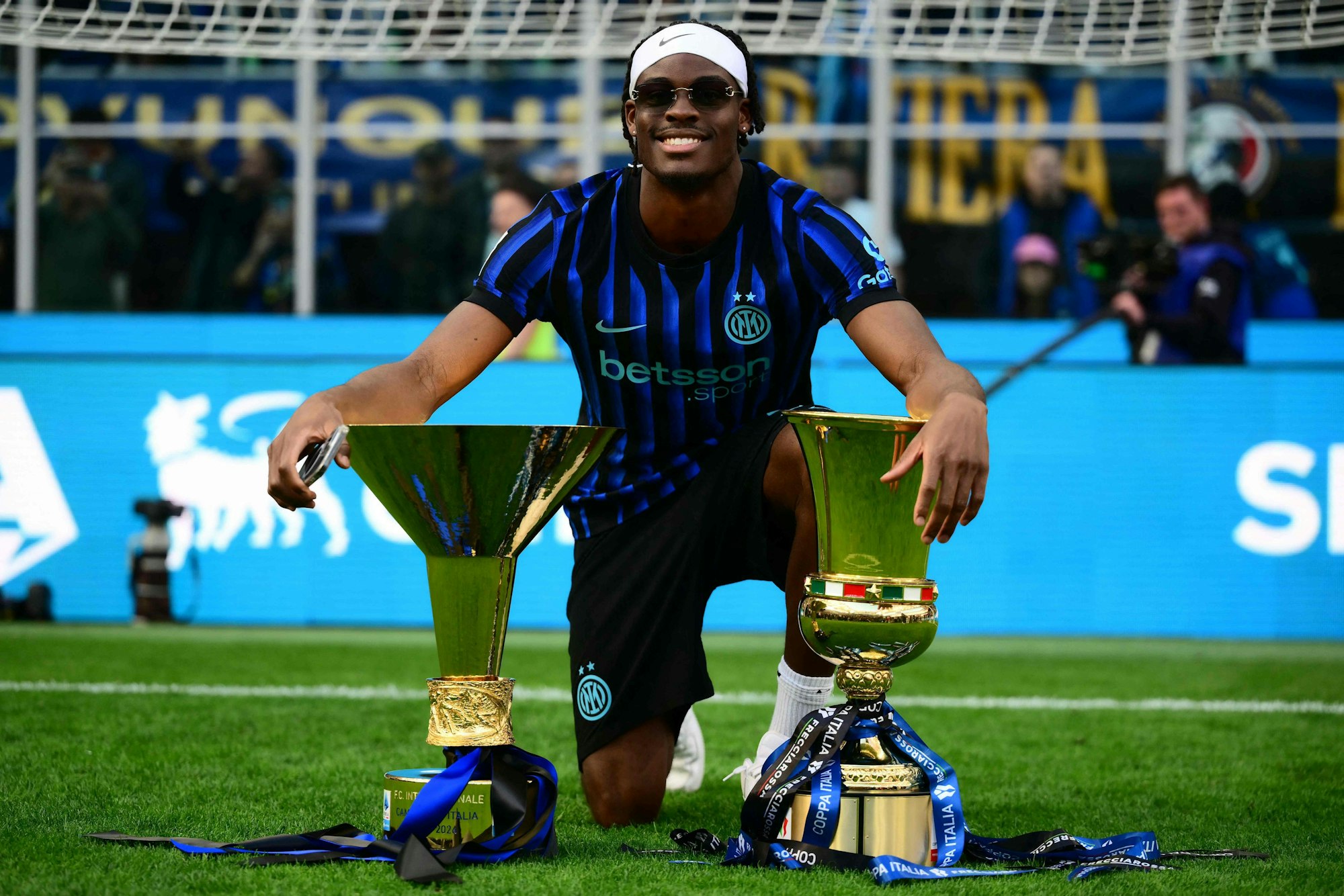 Yann Aurel Bisseck posiert mit zwei Trophäen auf dem Spielfeld.