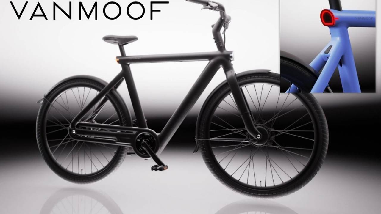 VanMoof S6 E-Bike in der Seitenansicht in der Farbe Drift Black vor hellem Hintergrund, mit Detailaufnahme des nahtlos in den Aluminiumrahmen integrierten Rücklichts in der Farbe Electric Blue – sichtbar auch das integrierte Frontlicht am Vorderrad.
