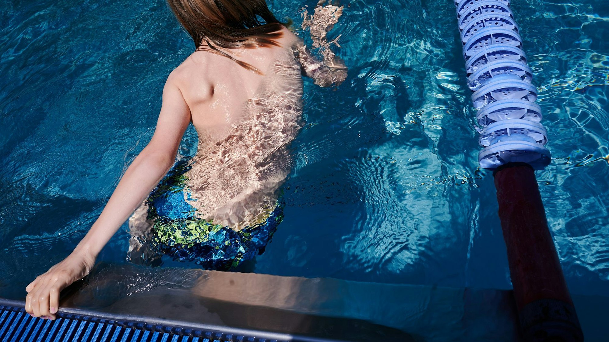 Ein Kind hält sich am Rand eines Schwimmbeckens fest