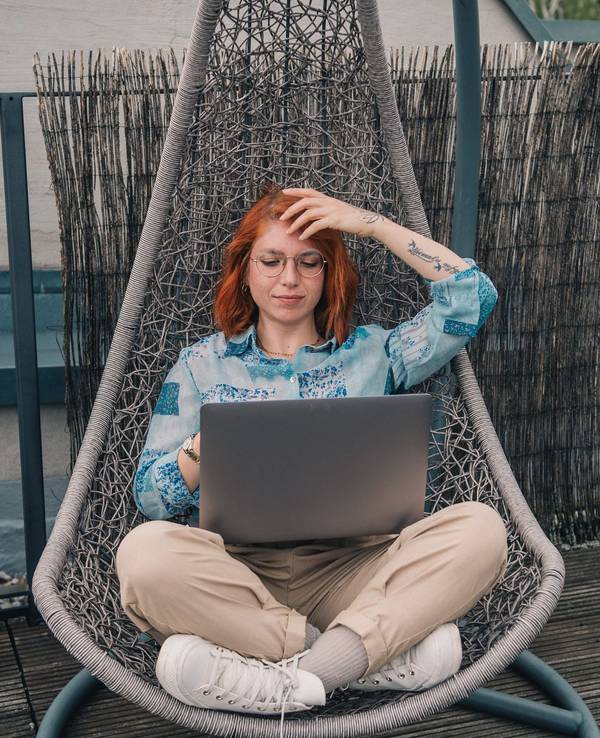 Eine Frau sitzt in einem Hängesessel und arbeitet am Laptop