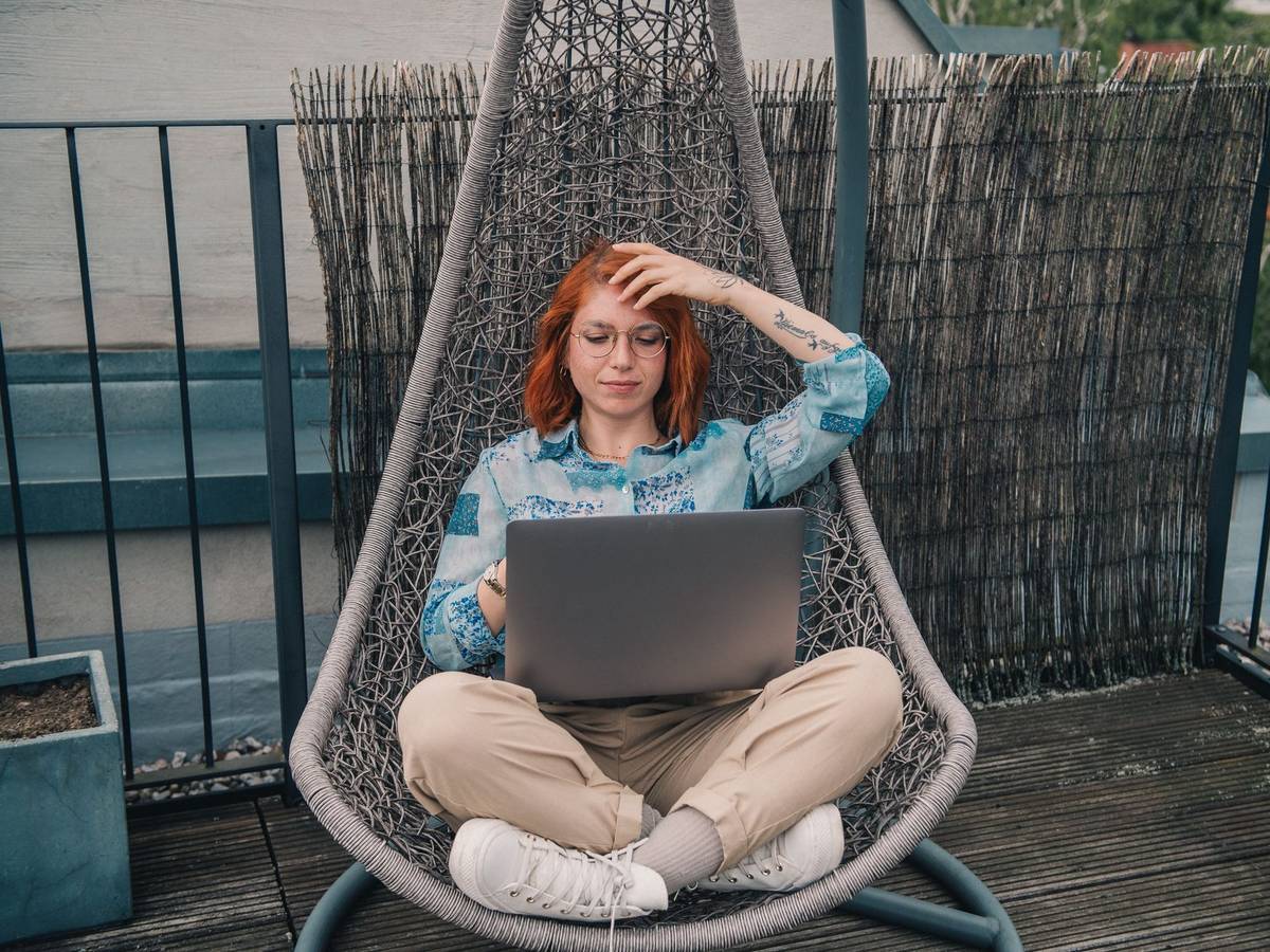 Eine Frau sitzt in einem Hängesessel und arbeitet am Laptop