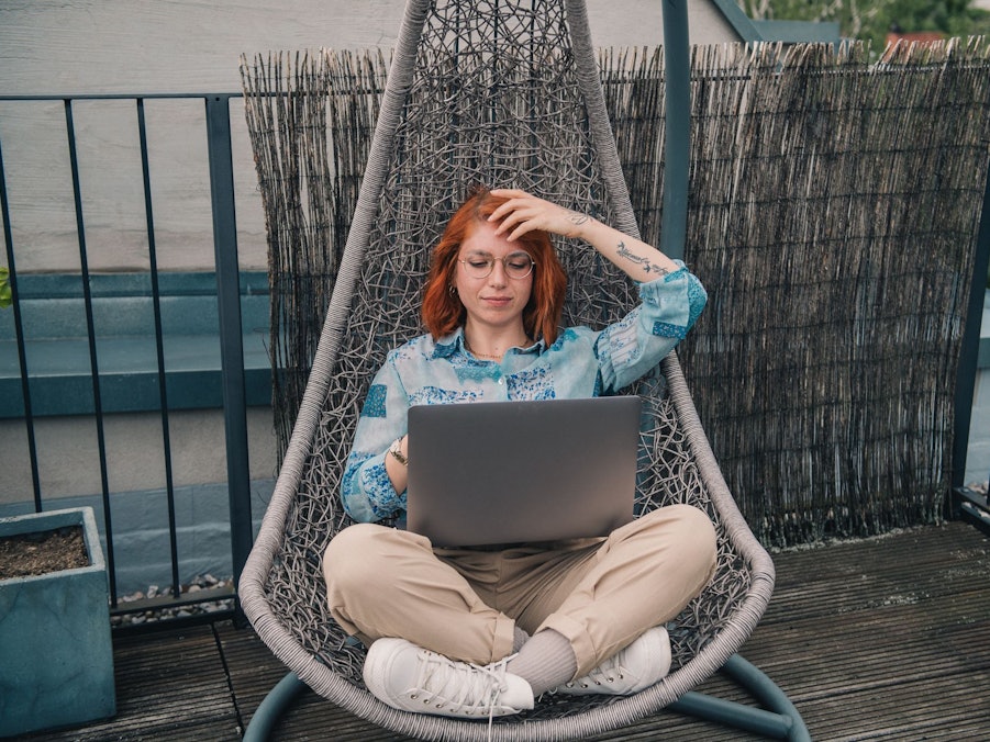 Eine Frau sitzt in einem Hängesessel und arbeitet am Laptop