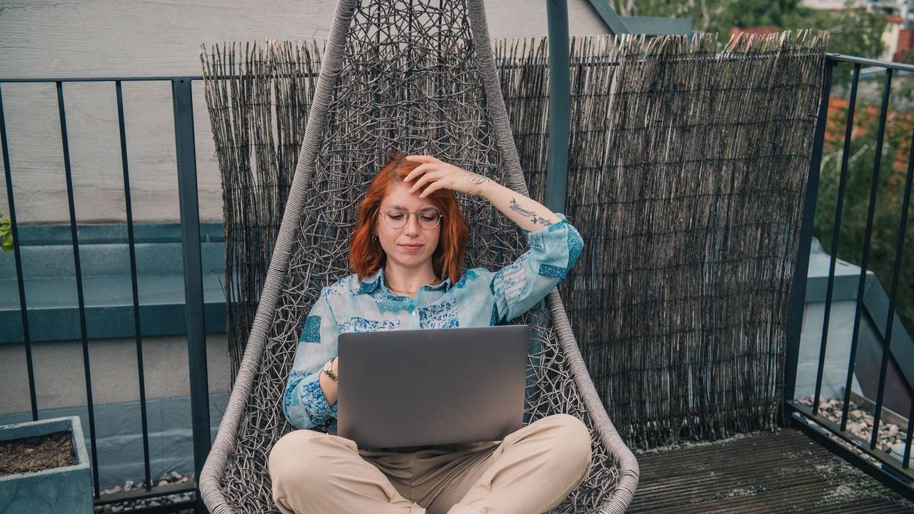 Eine Frau sitzt in einem Hängesessel und arbeitet am Laptop