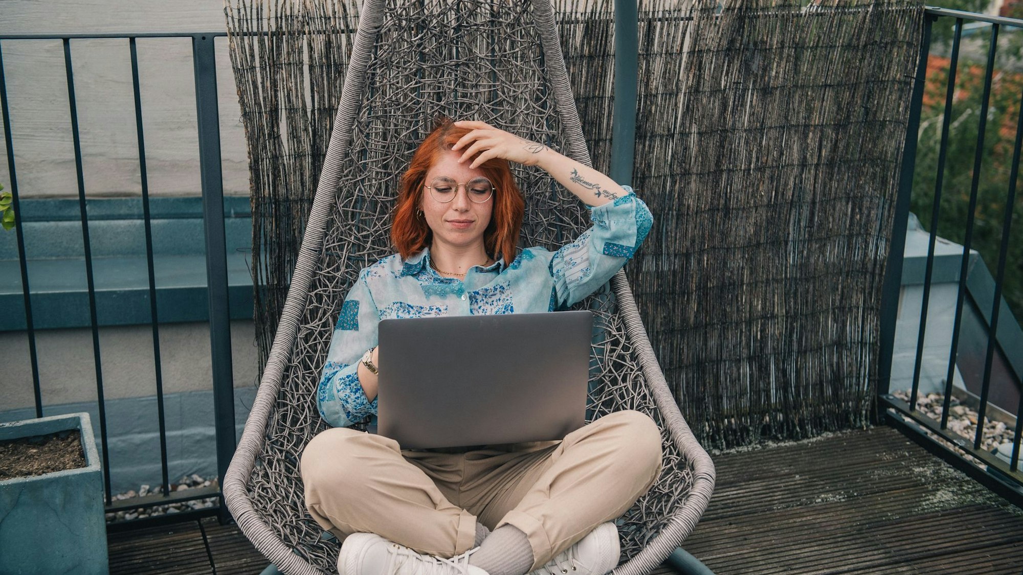 Eine Frau sitzt in einem Hängesessel und arbeitet am Laptop