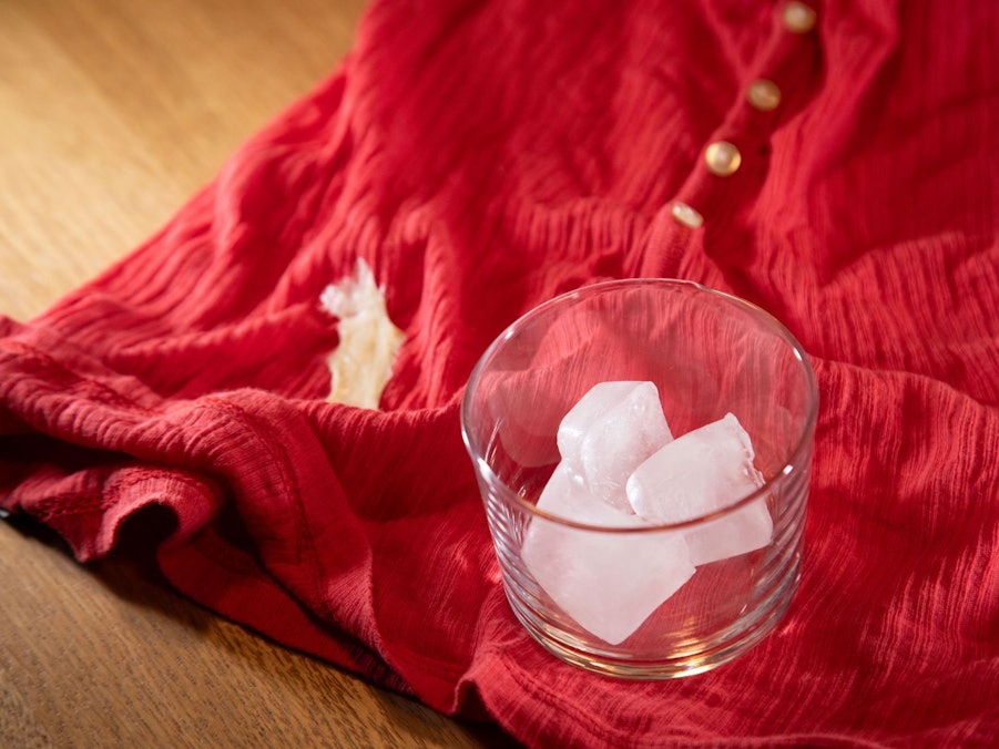 Glas mit Eiswürfeln steht auf einem Shirt mit Kaugummi-Fleck