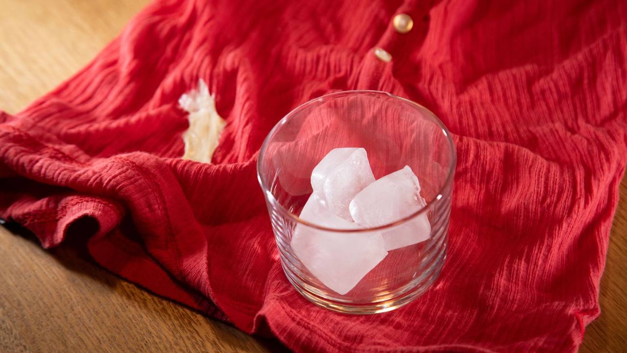 Glas mit Eiswürfeln steht auf einem Shirt mit Kaugummi-Fleck