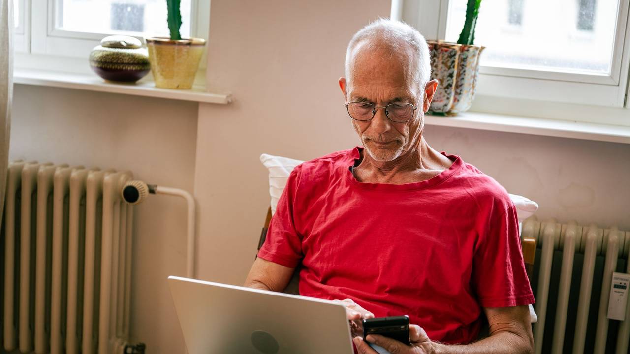 Ein Senior sitzt mit Laptop und Smartphone auf einem Sessel