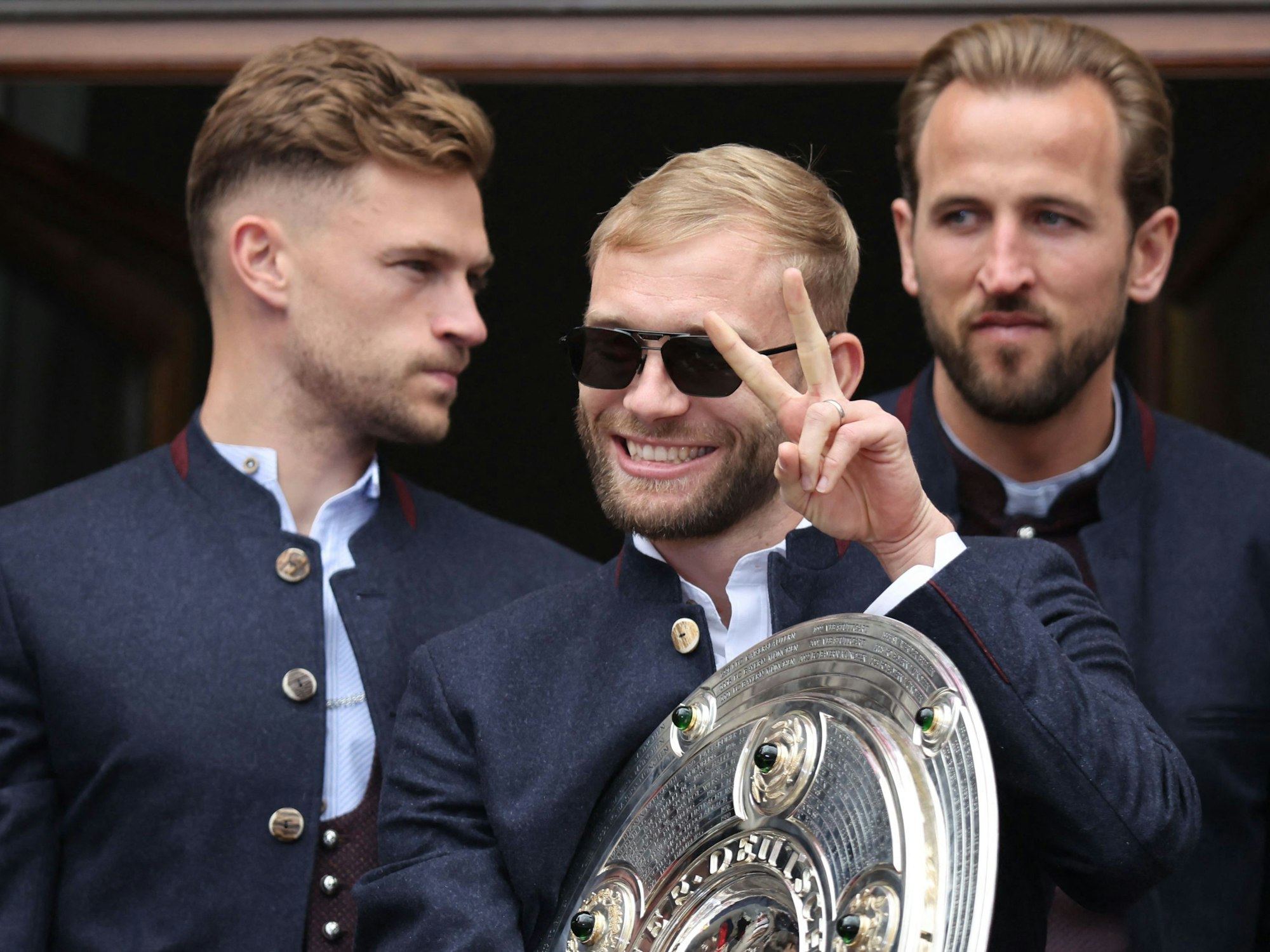 Konrad Laimer vom FC Bayern feiert mit der Meisterschale. DFB-Profi Joshua Kimmich und England-Kapitän Harry Kane stehen dahinter.