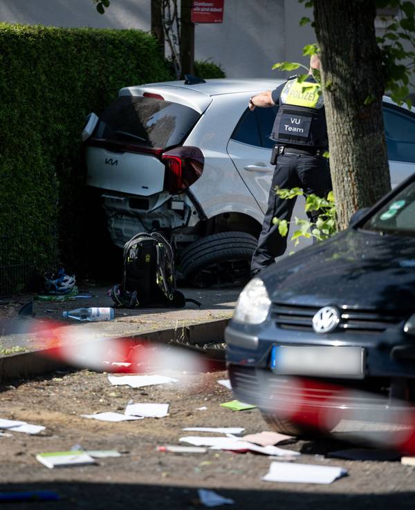 Ein Schulrucksack liegt auf dem Boden vor beschädigten Autos. Die Polizei sichert eine Unfallstelle, nachdem eine Autofahrerin drei Kinder vor einer Schule in Dinslaken verletzt hat