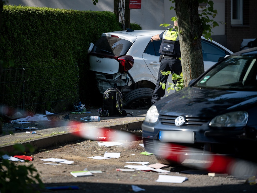 Ein Schulrucksack liegt auf dem Boden vor beschädigten Autos. Die Polizei sichert eine Unfallstelle, nachdem eine Autofahrerin drei Kinder vor einer Schule in Dinslaken verletzt hat