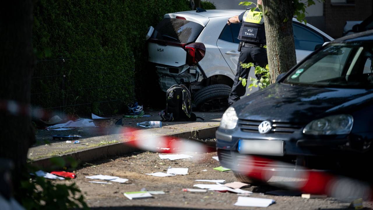 Ein Schulrucksack liegt auf dem Boden vor beschädigten Autos. Die Polizei sichert eine Unfallstelle, nachdem eine Autofahrerin drei Kinder vor einer Schule in Dinslaken verletzt hat
