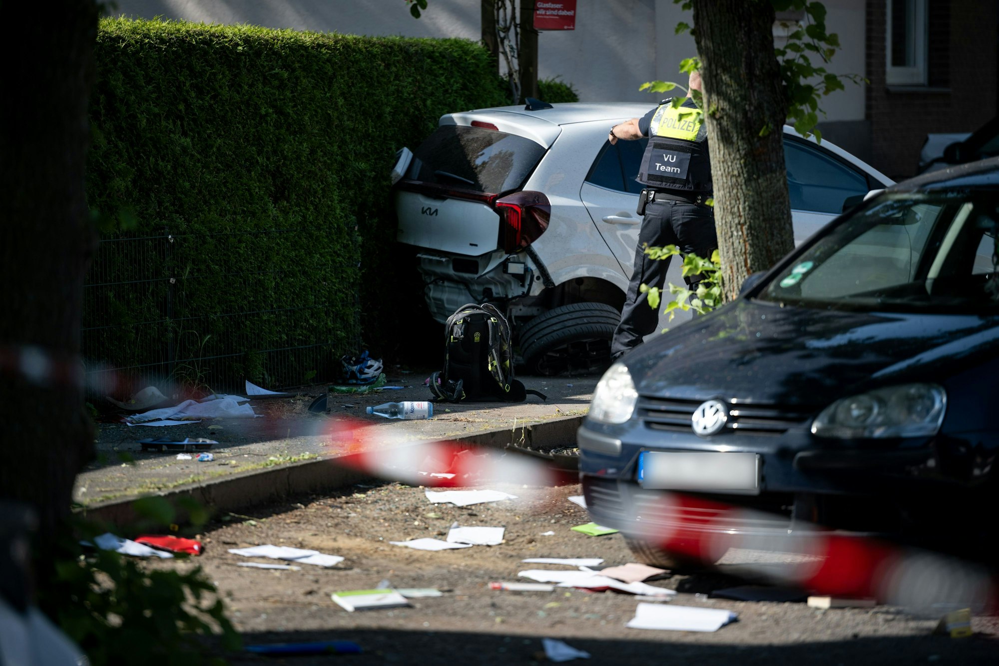 Ein Schulrucksack liegt auf dem Boden vor beschädigten Autos. Die Polizei sichert eine Unfallstelle, nachdem eine Autofahrerin drei Kinder vor einer Schule in Dinslaken verletzt hat