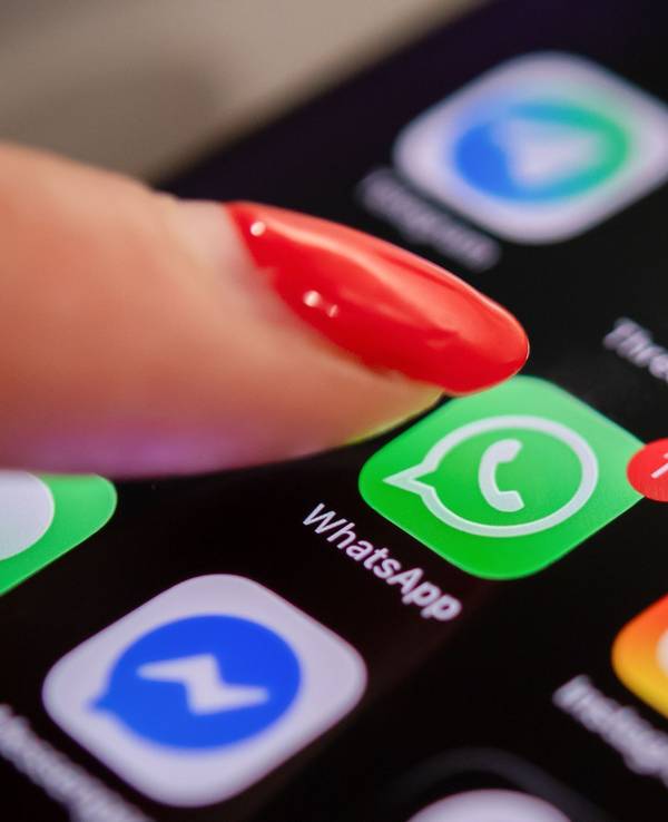 Eine Frau tippt auf einem Smartphone auf das WhatsApp-Symbol