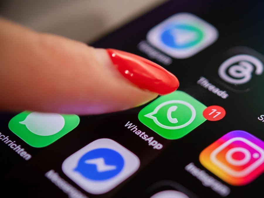Eine Frau tippt auf einem Smartphone auf das WhatsApp-Symbol